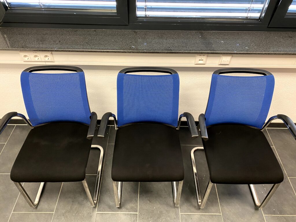 Drei Bürostühle mit blauer Netzrückenlehne und schwarzem Polstersitz, vor einem Fenster mit Granit-Fensterbank.