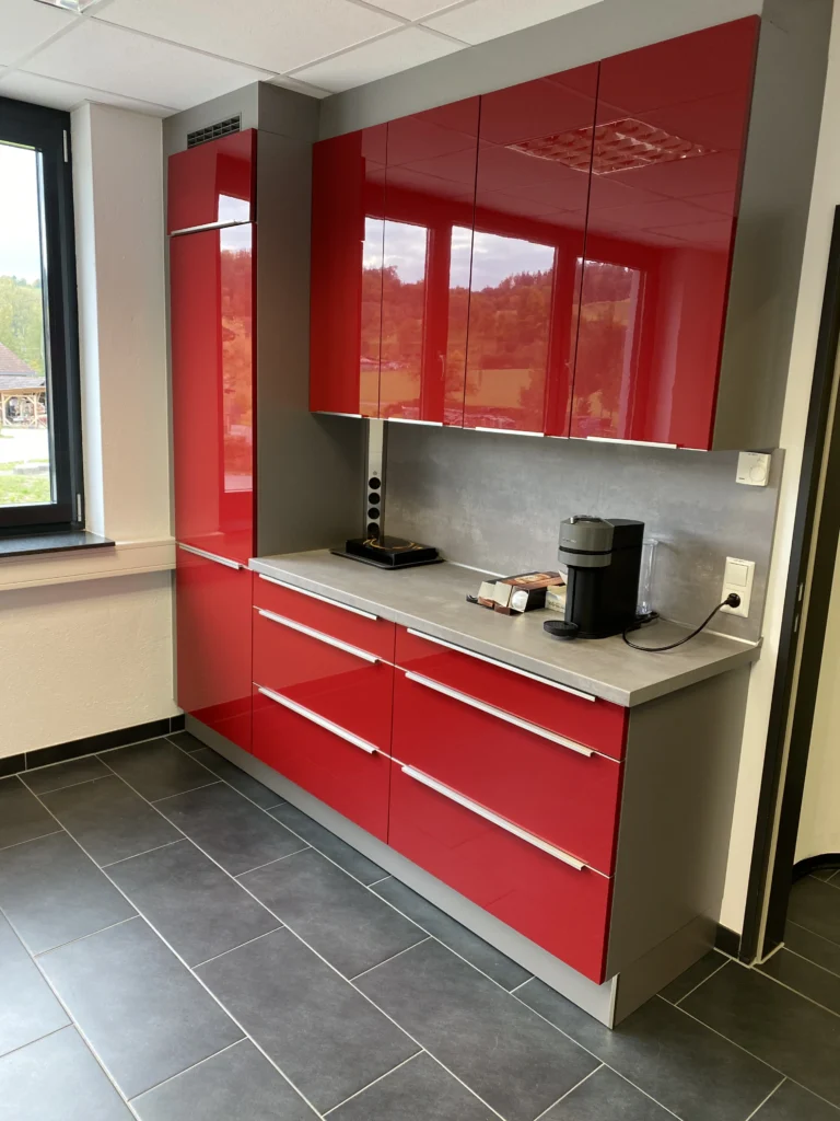 Moderne Büroküche mit roten Hochglanzfronten und grauer Arbeitsplatte.