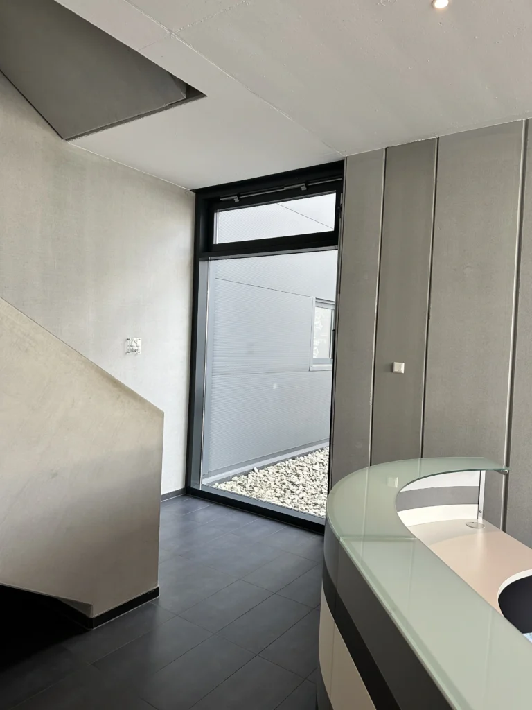 Moderne Empfangshalle mit stilvoller Rezeption, minimalistischer Wandgestaltung und einer großen Glastür für natürlichen Lichteinfall.
