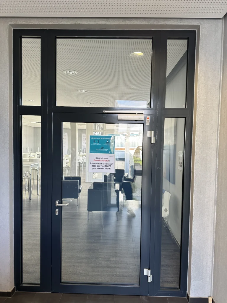 Moderne Glastür als Eingang zu einem Gewerbegebäude mit einer Informationsnotiz auf der Tür.