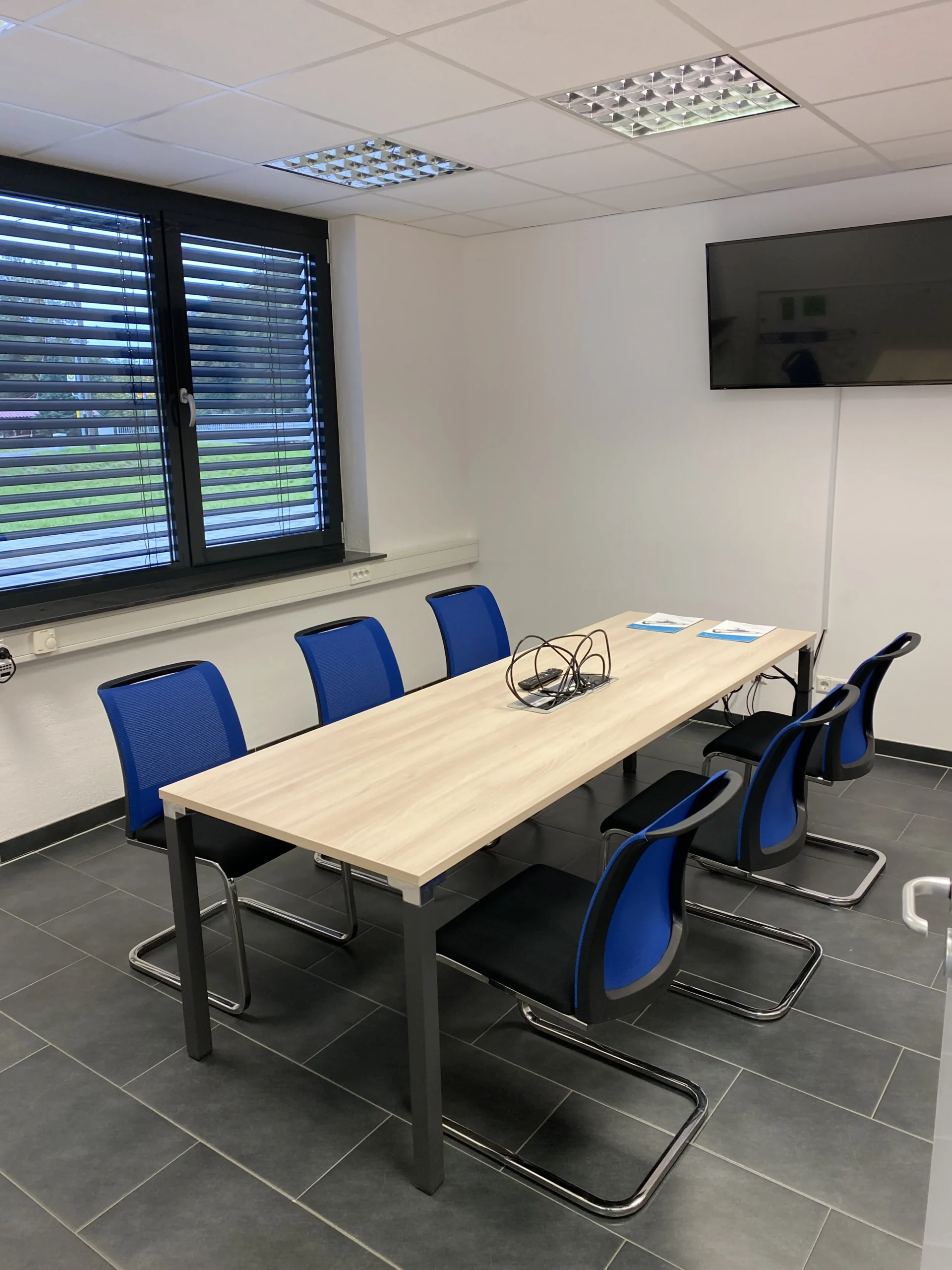 Konferenzraum mit Besprechungstisch und blauen Stühlen Moderner Konferenzraum mit einem langen Besprechungstisch aus Holz, sechs blauen Stühlen und einer Wandmontierten TV-Bildschirm.