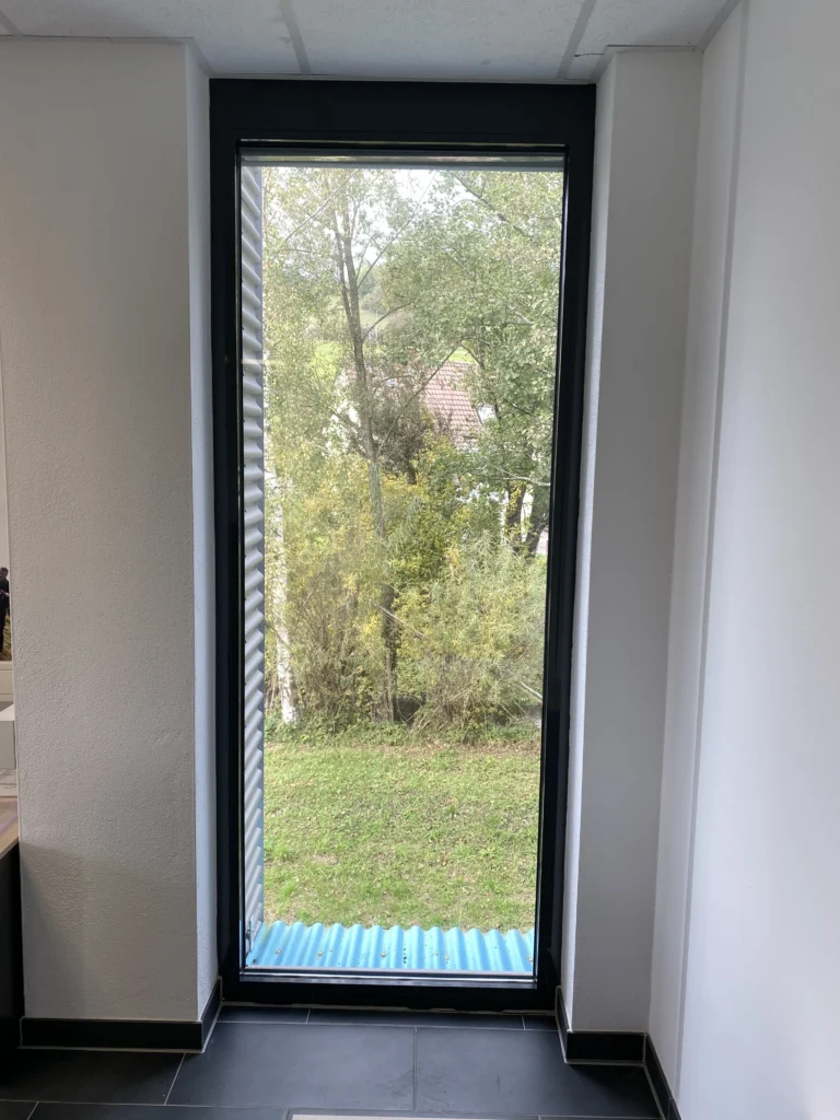 Modernes Bürofenster mit schwarzem Rahmen und Blick ins Grüne.