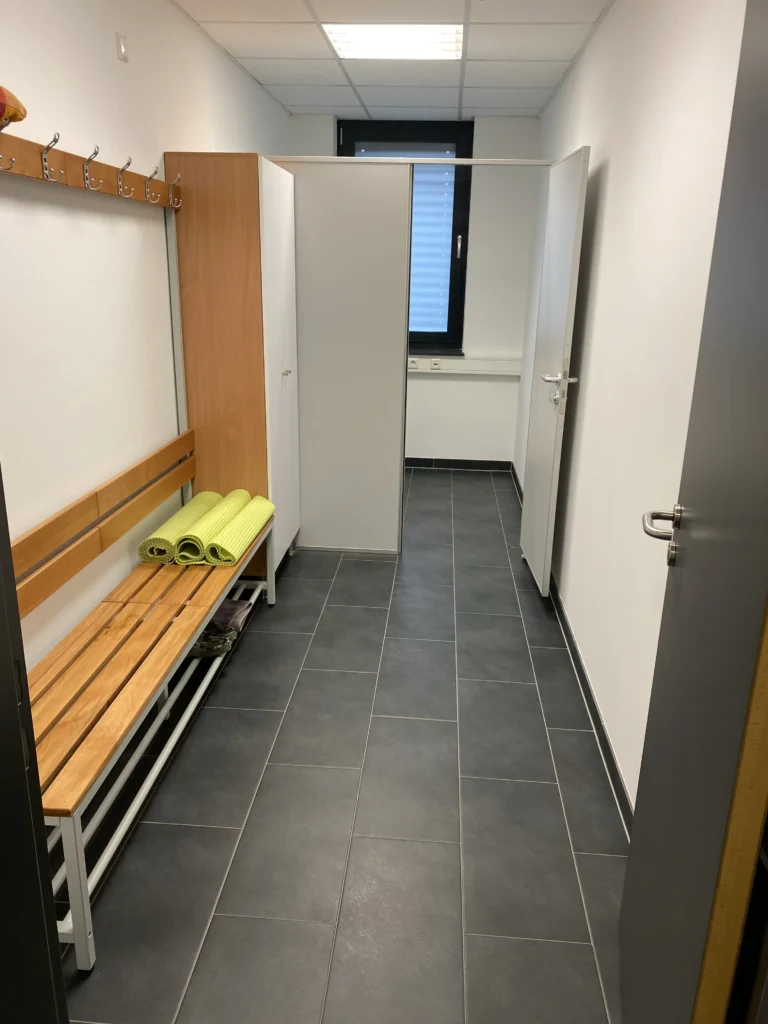 Umkleideraum mit Holzbänken, Spinden und Umkleidekabinen in einem modernen Gebäude.