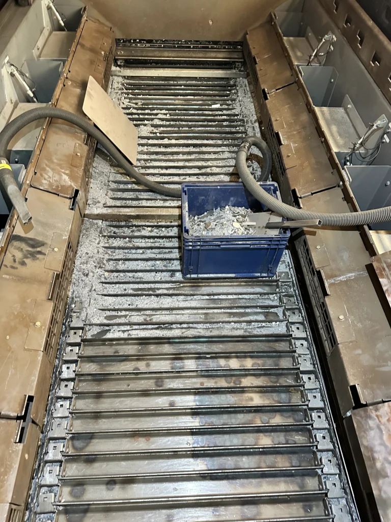 Reinigung einer Laserschneidanlage mit Industriesaugern und einer Box zur Sammlung von Metallstaub und Schneidabfällen.