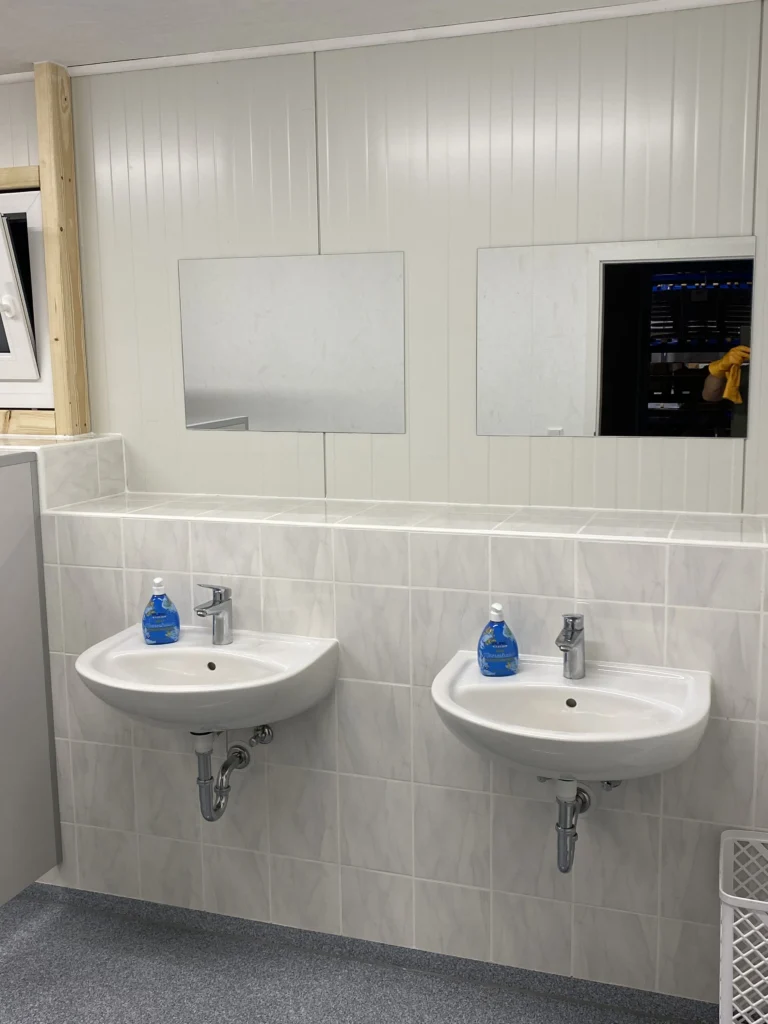 Zwei weiße Waschbecken mit Spiegeln in einem Waschraum.