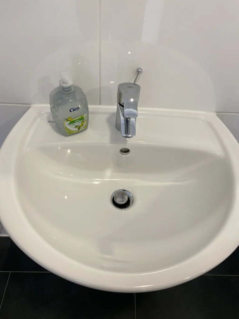 Weißes Waschbecken mit verchromtem Wasserhahn und Seifenspender in einem modernen Badezimmer.